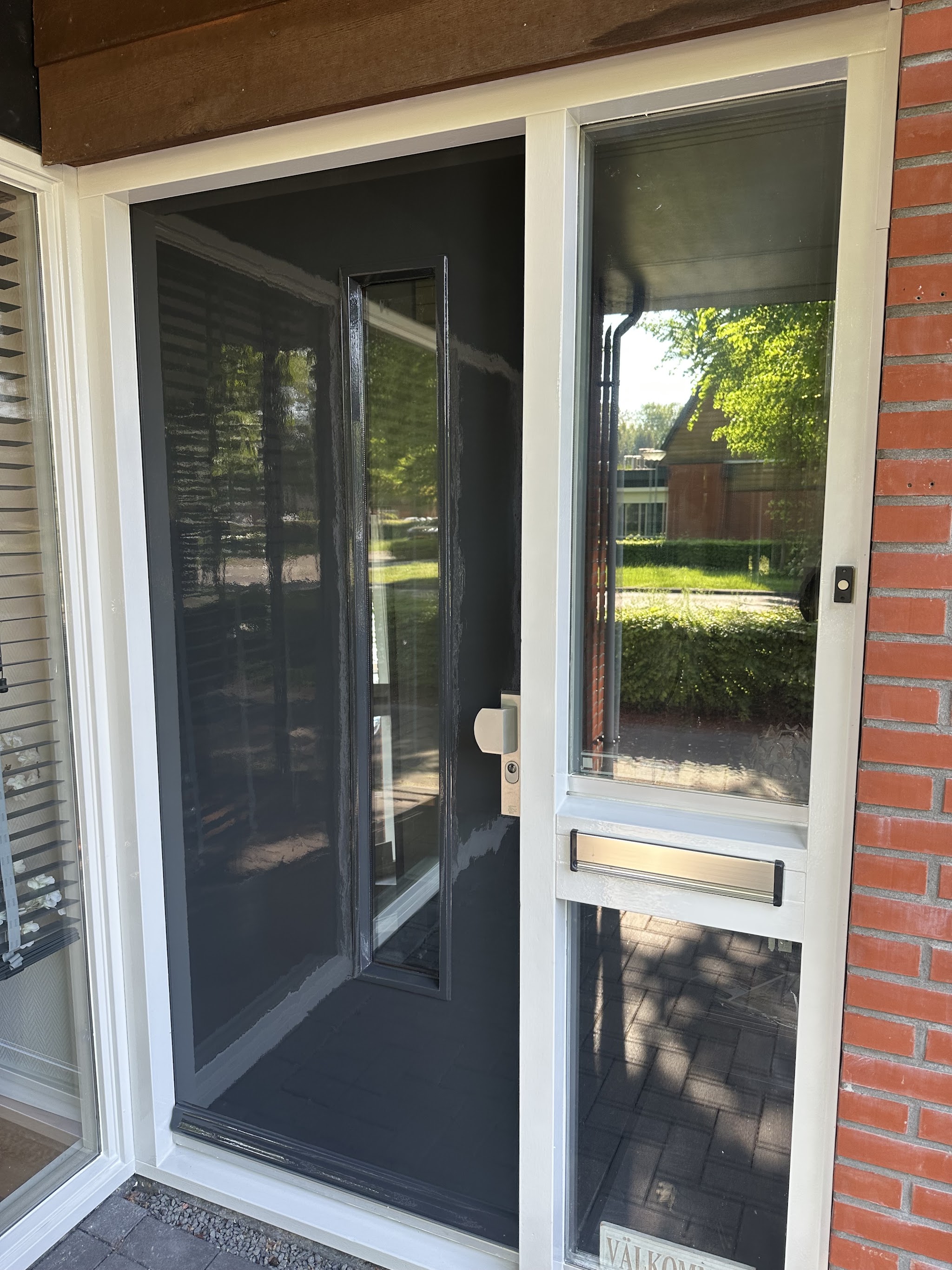 Vers geschilderde donkergrijze voordeur met glaspaneel en wit kozijn in een bakstenen gevel