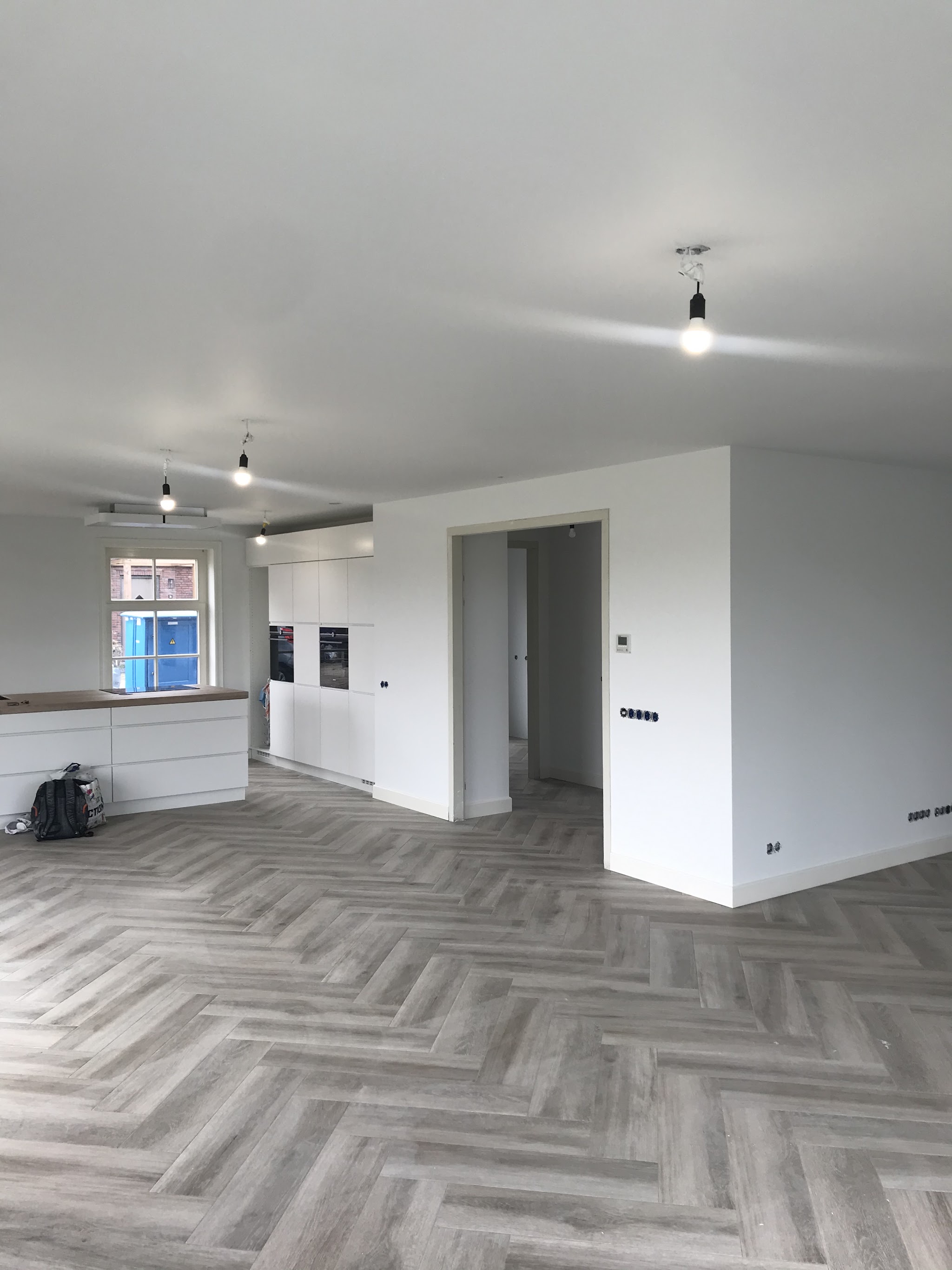 Lege woonkamer met open keuken, witte wanden en een visgraatvloer