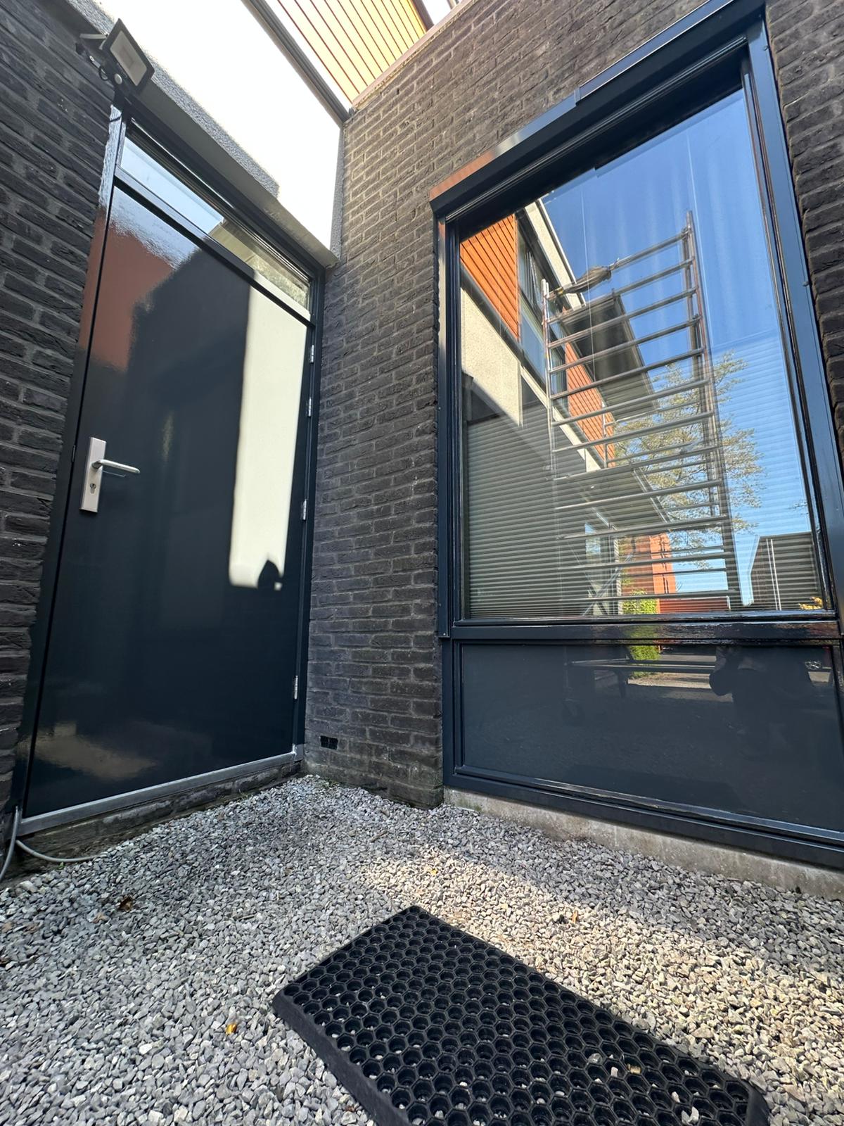 Donker geschilderd kozijn en deur in een hoek van baksteen, vers in de lak