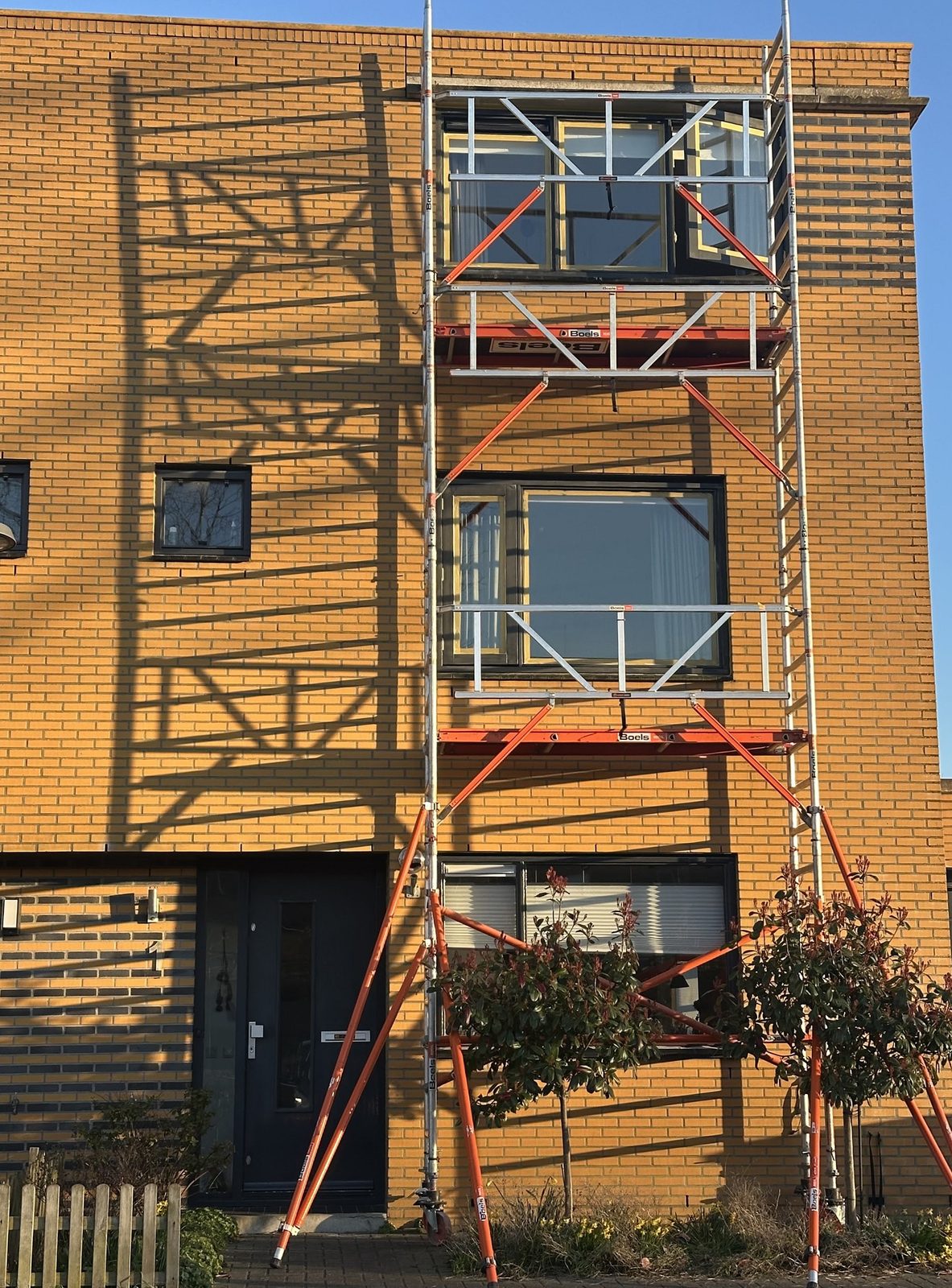 Rijtjeshuis van oranje baksteen met een steiger voor de gevel, kozijnen in voorbereiding